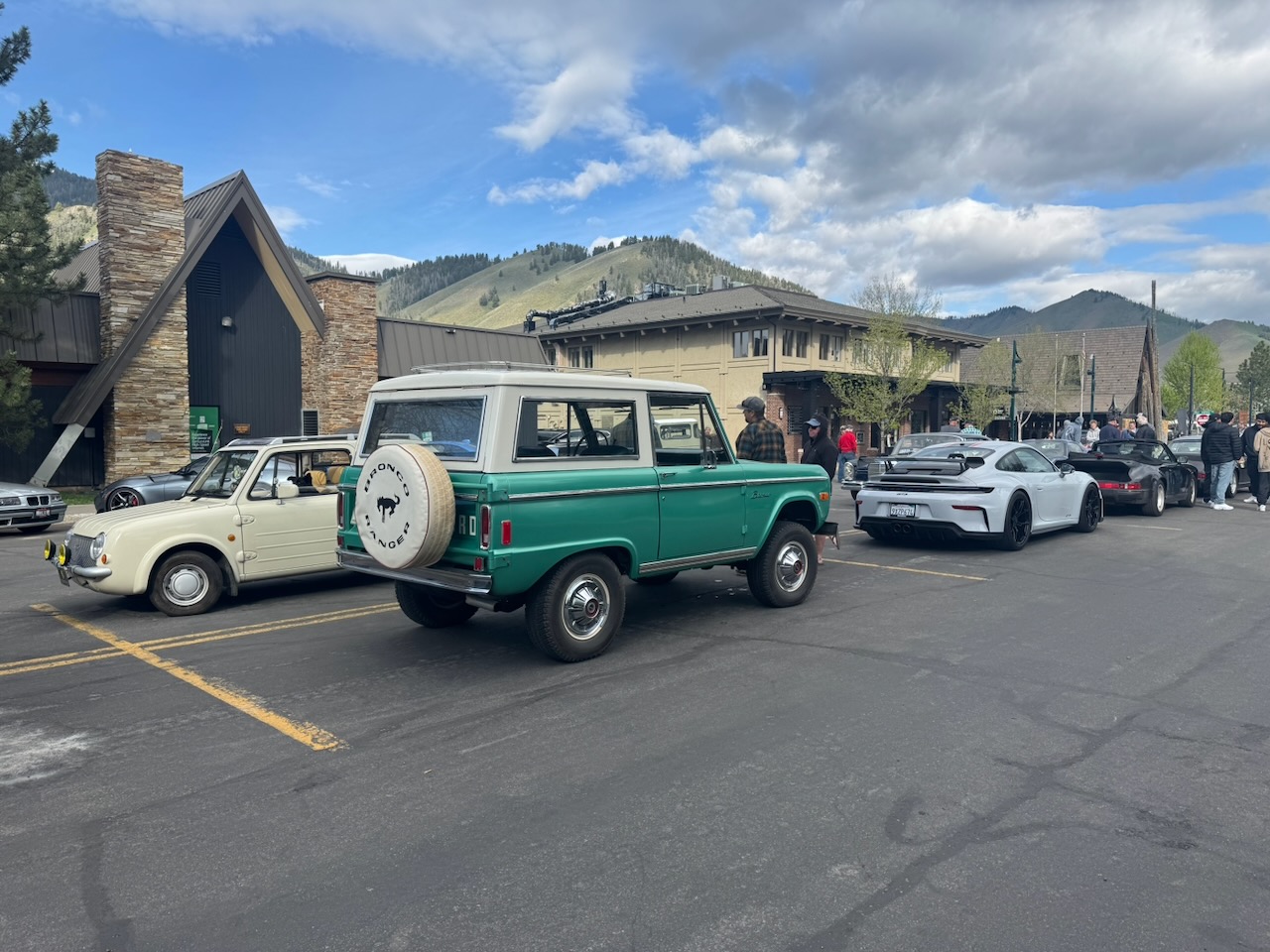 Classic cars, a green Bronco, and modern sports cars at a Ketchum gathering with mountains behind them